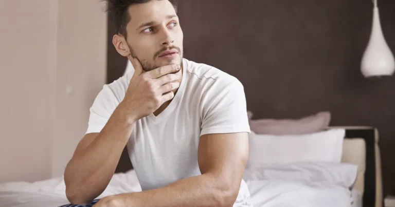 Homme pensif assis au bord du lit le matin, image d'une baisse de libido masculine