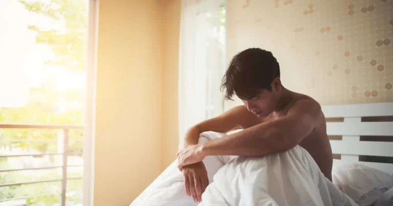 Homme pensif assis au bord du lit, symbole de l'inquiétude liée à l'éjaculation précoce