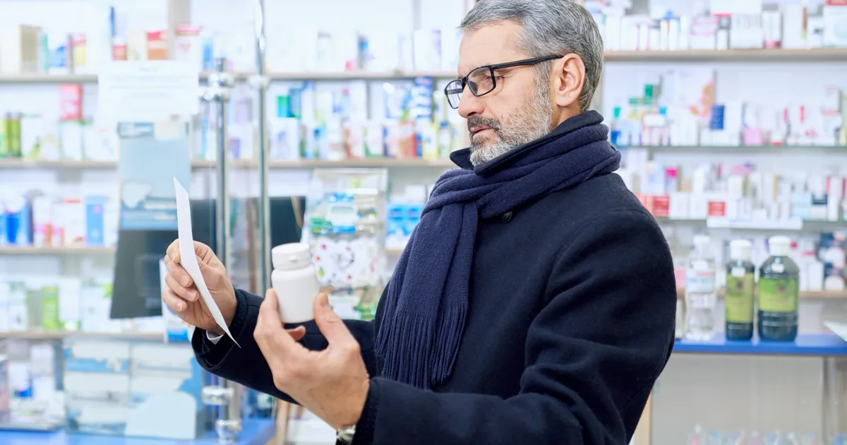 Homme qui lit l'étiquette d'un complément alimentaire pour l'érection avant de l'acheter en pharmacie