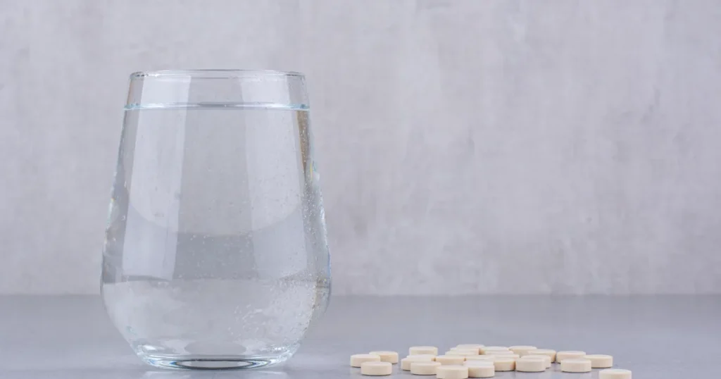 Gélules de L-arginine posées à côté d'un verre d'eau, prises en cure pour soutenir l'érection