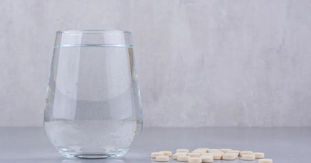 Gélules de L-arginine posées à côté d'un verre d'eau, prises en cure pour soutenir l'érection